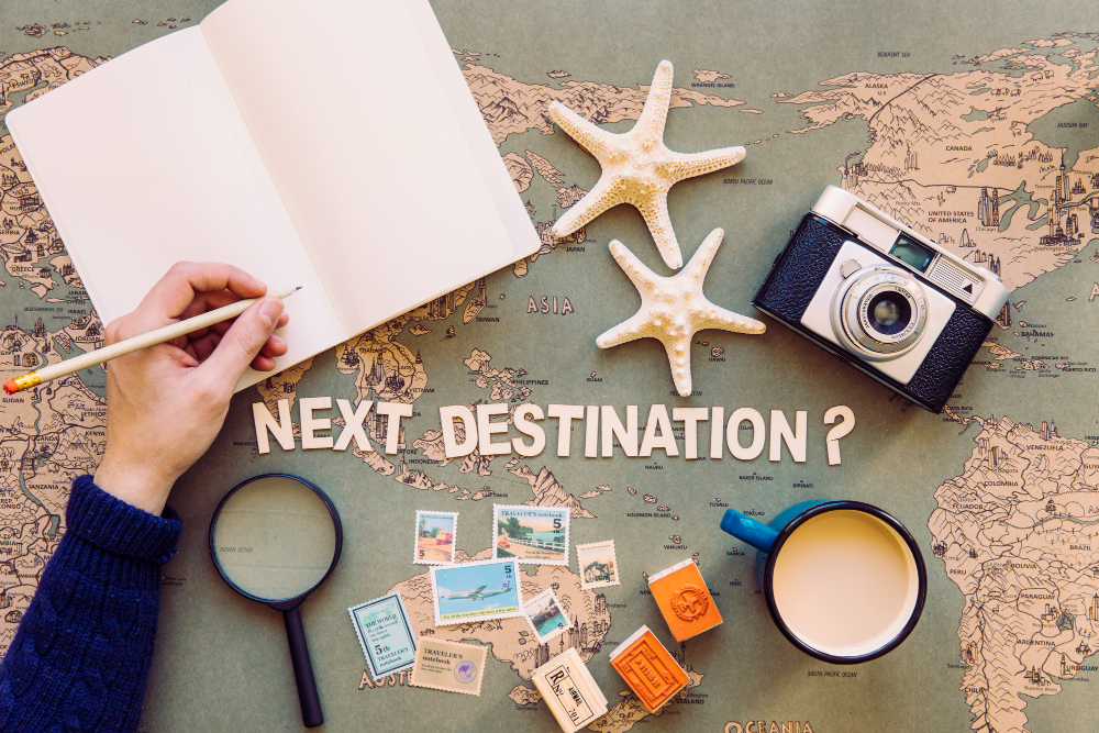 A flat-lay of travel essentials around the words 'Next Destination?'